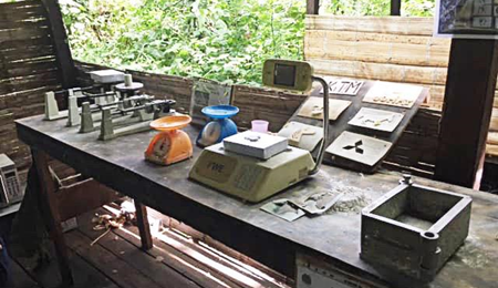 Se observa un laboratorio clandestino de procesamiento de cocaína en la selva. El laboratorio es rústico, está en una estructura de madera y cuenta con equipos y materiales para procesar, marcar y empacar la cocaína.