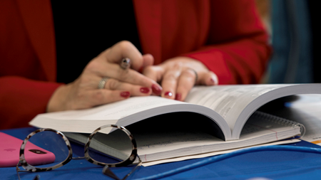 A woman's hands over an open book, with a pair of glasses in the foreground