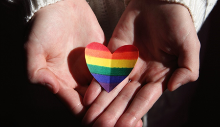 Manos sosteniendo un corazón con los colores de la bandera LGBTI 