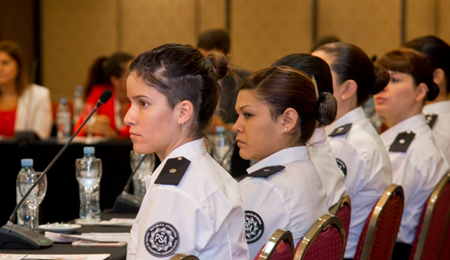 Six female officers of the Argentine Airport Security Police participate in the GENLEA National Workshop in Buenos Aires, which took place in February 2019. The women are seated at a round table, facing left, paying attention to a presentation.
